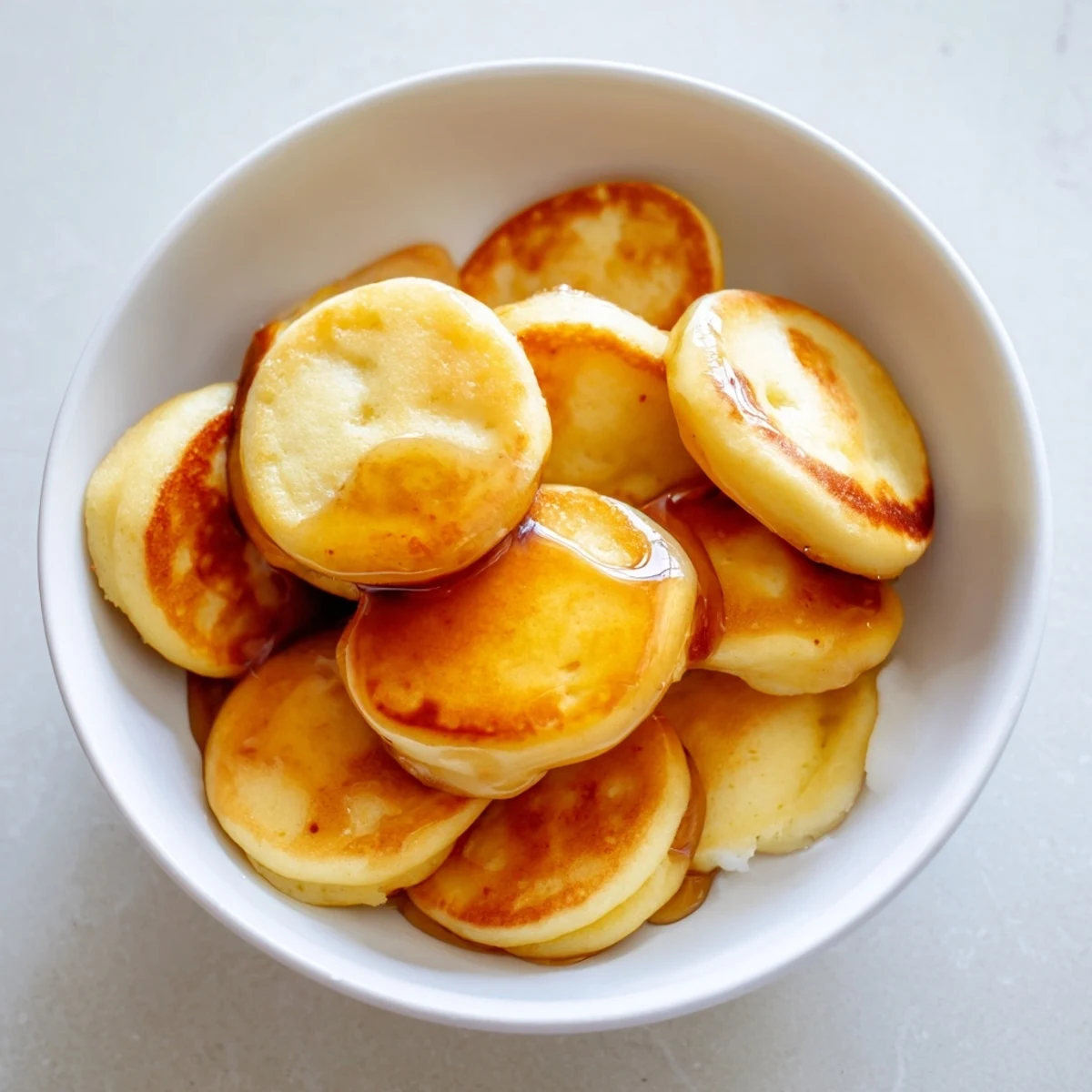 Pile of golden brown fluffy pancake cereal in a serving bowl with maple syrup.