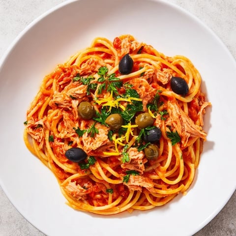 Golden ribbons of pasta with tuna, olives, & capers simmer in a rich tomato sauce, ready to serve.