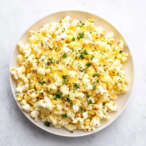 Golden, fluffy savoury popcorn mixes tossed with vibrant herbs and Parmesan cheese, ready to enjoy.