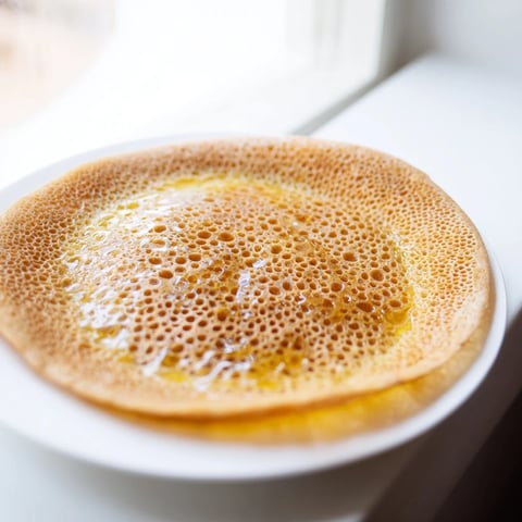 Golden, porous Moroccan Baghrir crepes are dripping with warm honey butter, a delightful breakfast treat.