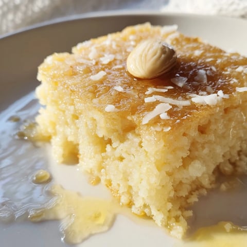 Golden-brown Basbousa cake, a moist Egyptian dessert, drizzled with sweet syrup and topped with almonds.
