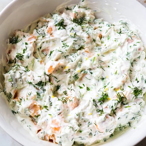 A close-up of creamy smoked salmon dip topped with fresh dill and lemon wedges, served in a rustic bowl.  