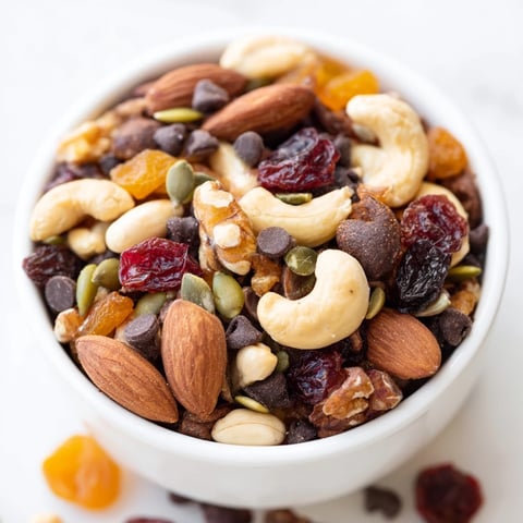 A close-up of homemade trail mix custom with almonds, cashews, dark chocolate chips, dried cranberries, and pumpkin seeds in a rustic bowl.  