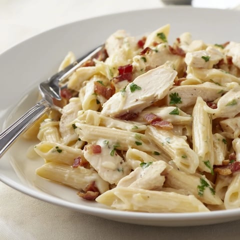 A close-up of creamy chicken bacon penne served in a white bowl, garnished with fresh parsley and extra Parmesan.