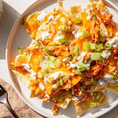 Golden Buffalo Chicken Nachos topped with melted cheddar, Monterey Jack, and a cool ranch drizzle.
