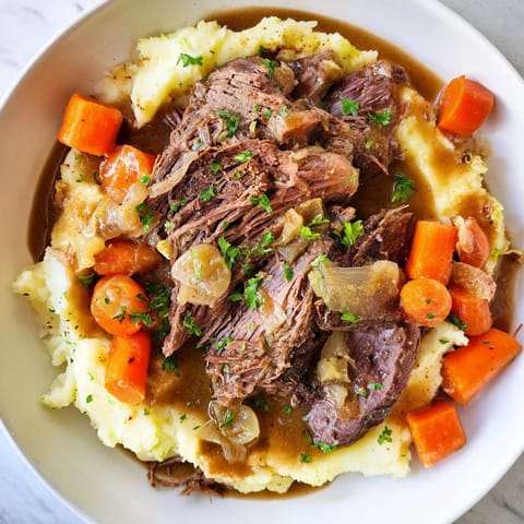 A close-up of a flavorful Slow Cooker Pot Roast with rich gravy served over fluffy potatoes.