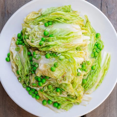 Steaming cabbage stir-fry with peas and a savory sauce glistens, a quick and easy vegetarian dish.