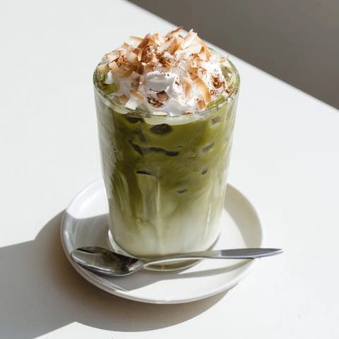 Golden toasted coconut sprinkled atop a refreshing Toasted Coconut Gingerbread Iced Matcha drink.