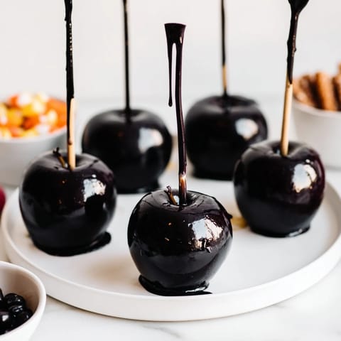 Dark, shimmering poison apples glistens next to a selection of Halloween treats on a party board.
