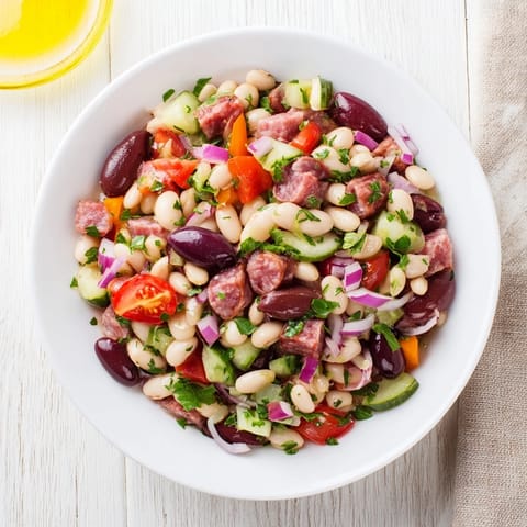 Close-up of a rustic bowl filled with fresh Mediterranean Dense Bean Salad and savory salami.