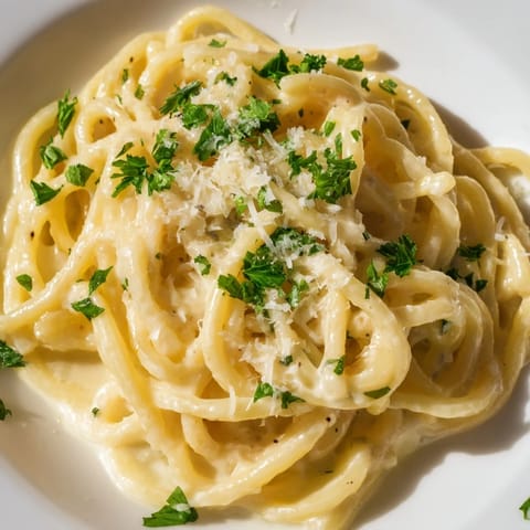 Golden-yellow Ramen Carbonara served hot, with parmesan cheese and fresh herbs as garnish.
