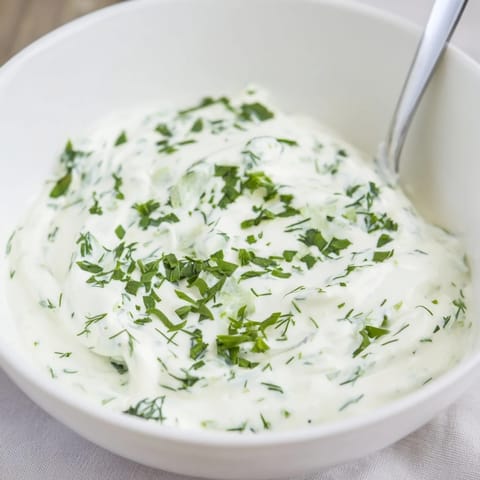 Creamy Greek Yogurt Herb Dip is spooned into a white bowl, surrounded by fresh vegetables and pita chips for dipping.  