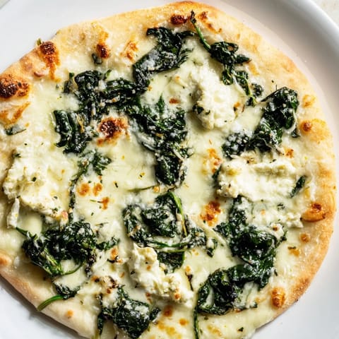 A slice of spinach ricotta pizza with garlic butter brushed on a crisp crust, topped with fresh spinach, ricotta, and a pinch of red pepper flakes.