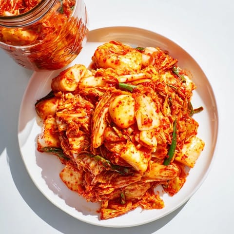 Freshly made kimchi packed in a glass jar, showcasing its bright orange spice paste coating shredded cabbage, carrots, and radishes during fermentation.  