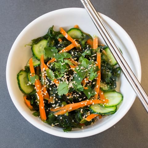 A close-up of vibrant Japanese seaweed salad with cucumber, carrot, and scallions in sesame-ginger dressing.