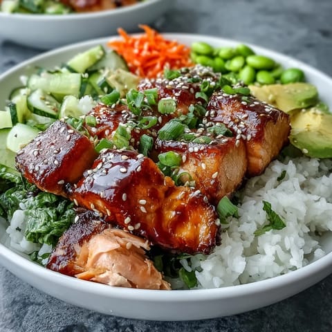 A close-up of the Baked Salmon Rice Bowl shows crisp cucumber slices, creamy avocado, and a drizzle of sriracha mayo over tender salmon.  