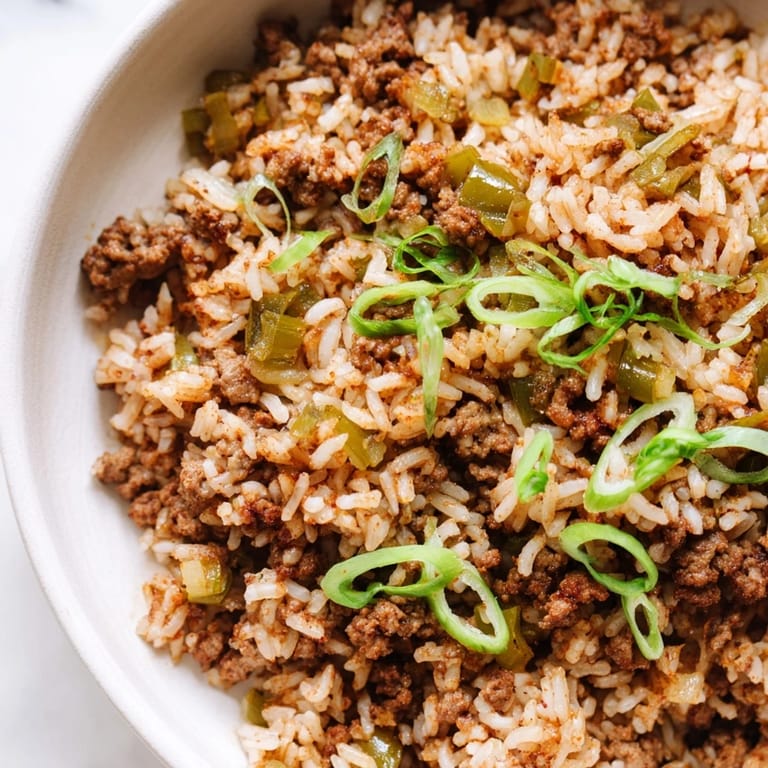 Close-up shot shows a fluffy plate of Cajun Dirty Rice with spices and fresh green onions.