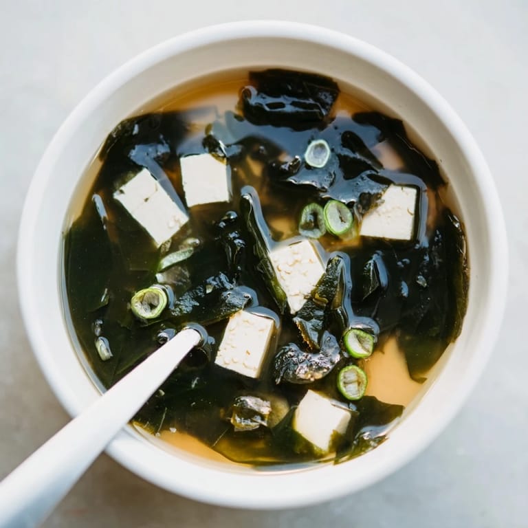 Close-up of wakame soup with vibrant green seaweed, white tofu, and sliced scallions over a dark backdrop, highlighting its mineral-rich, vegetarian, and low-calorie qualities.