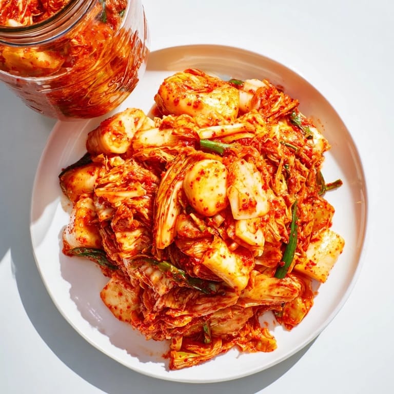 Freshly made kimchi packed in a glass jar, showcasing its bright orange spice paste coating shredded cabbage, carrots, and radishes during fermentation.  