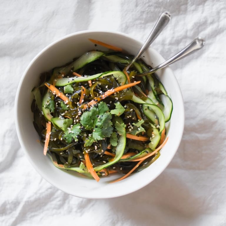 A refreshing bowl of vegan seaweed salad garnished with toasted sesame seeds and fresh cilantro, served as a light side.