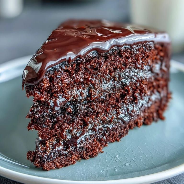 Rich Easy Chocolate Fudge Cake layers with glossy chocolate icing, paired with fresh raspberries for a vibrant contrast.