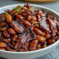 1. Summer BBQ baked beans with brown sugar and bacon in a cast-iron skillet, bubbling with sweet-smoky sauce and crispy bacon bits.  