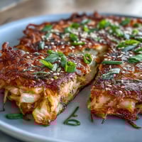 Crispy cabbage kimchi pancakes sizzling golden brown in a skillet, packed with tangy fermented vegetables.  